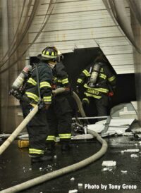 Firefighters move hoslines through hole cut into roll-down door