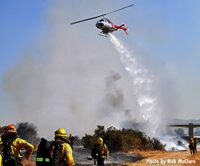 Firefighters observe helicopter making a drop on vegetation fire