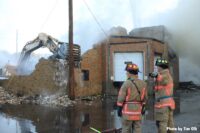 Firefighters with excavator in background knocking down building