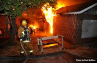 A firefighter with an uncharged hoseline observes raging house fire