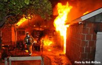 A firefighter at work as flames shoot from a structure