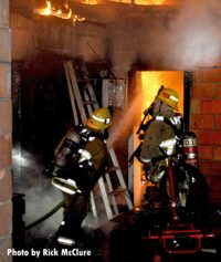 A firefighter blasts water through a doorway on flames