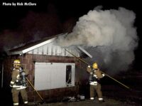 A firefighter uses a hook to open up on the outside of a building as smoke pumps out of the structure