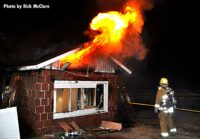 A firefighter with a hook and flames venting from the building