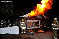 Flames shoot out from under the roof of the fire