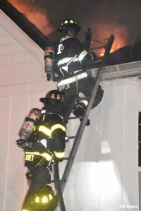 Firefighters ascend a ladder to roof of burning home