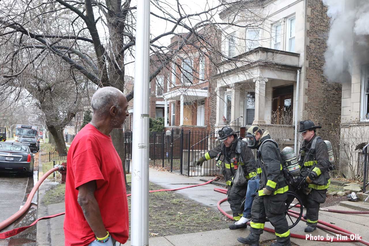 Chicago firefighters pull a victim from a fire as a civilian bystander looks on