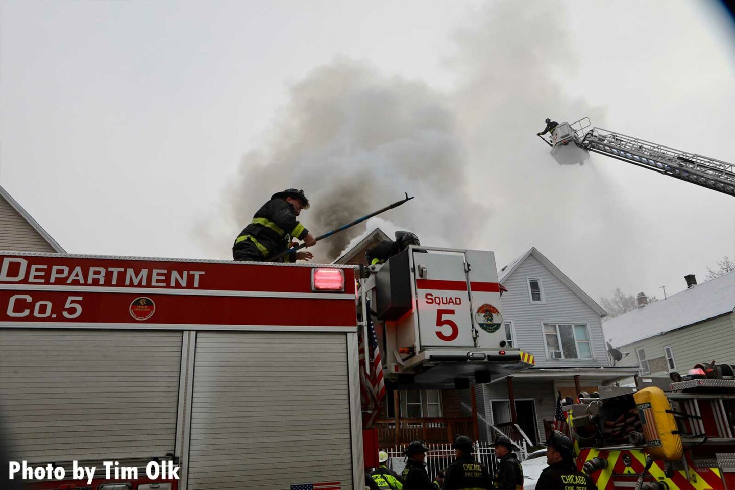 Chicago firefighter with a hook atop Squad 5 with Chicago firefighter in a tower ladder bucket in the background