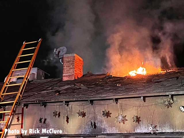 Flames emerge from the roof of the burning home