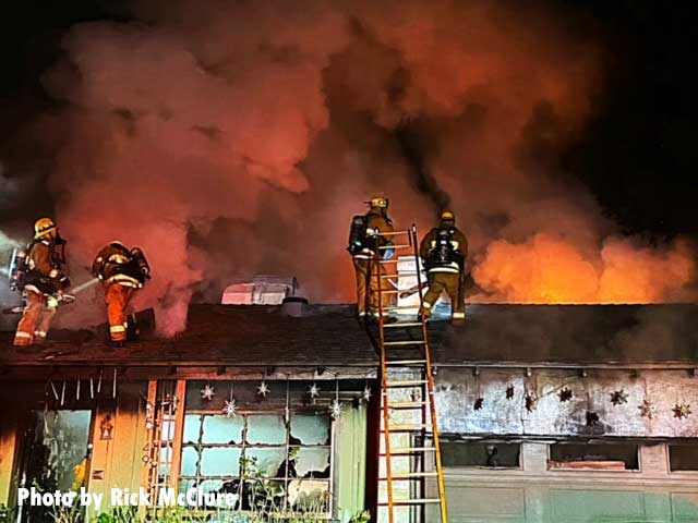 Four firefighters on the roof with a ladder and smoke showing