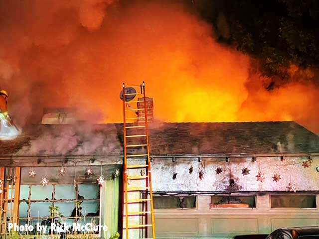 The light from flames on the roof with smoke and a ladder