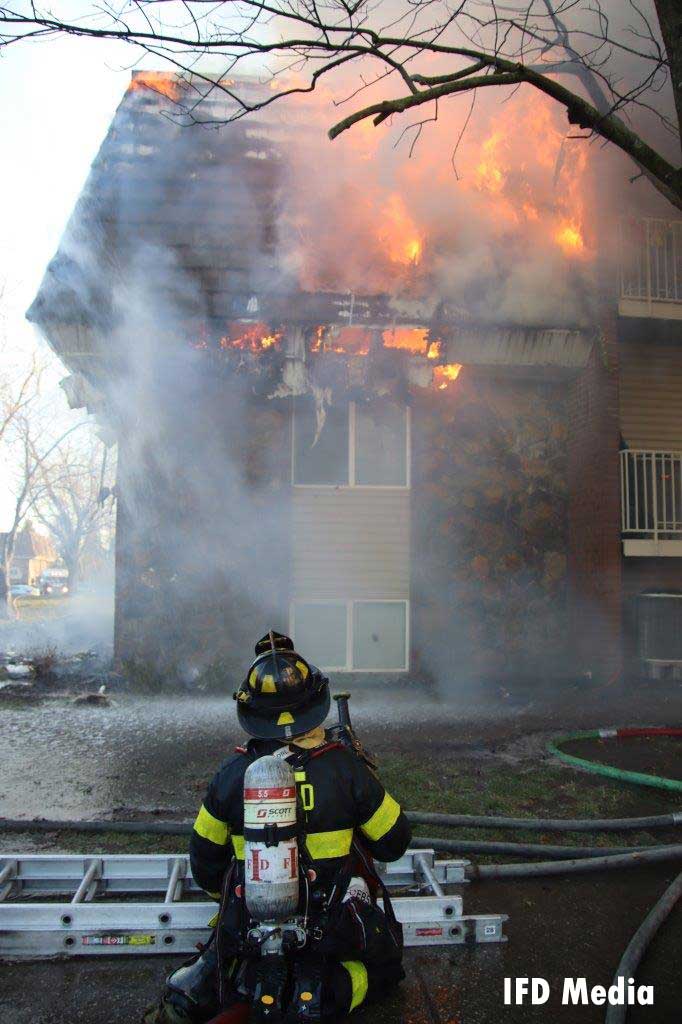 Firefighter with a ladder observing flames shooting from an apartment building