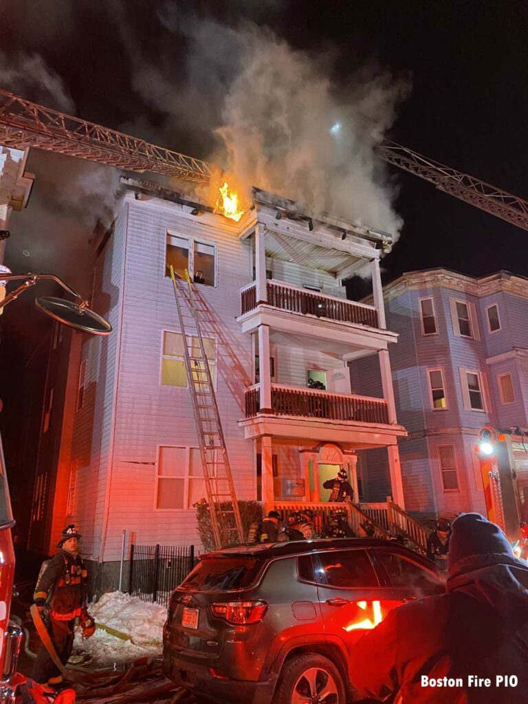 Multiple aerials in use as flames shoot from the top of the dwelling and a ground ladder on the building