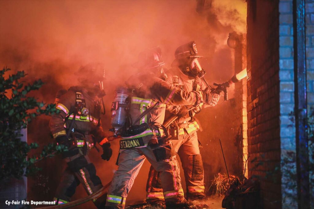 Firefighters train a hoseline onto the interior of a house fire