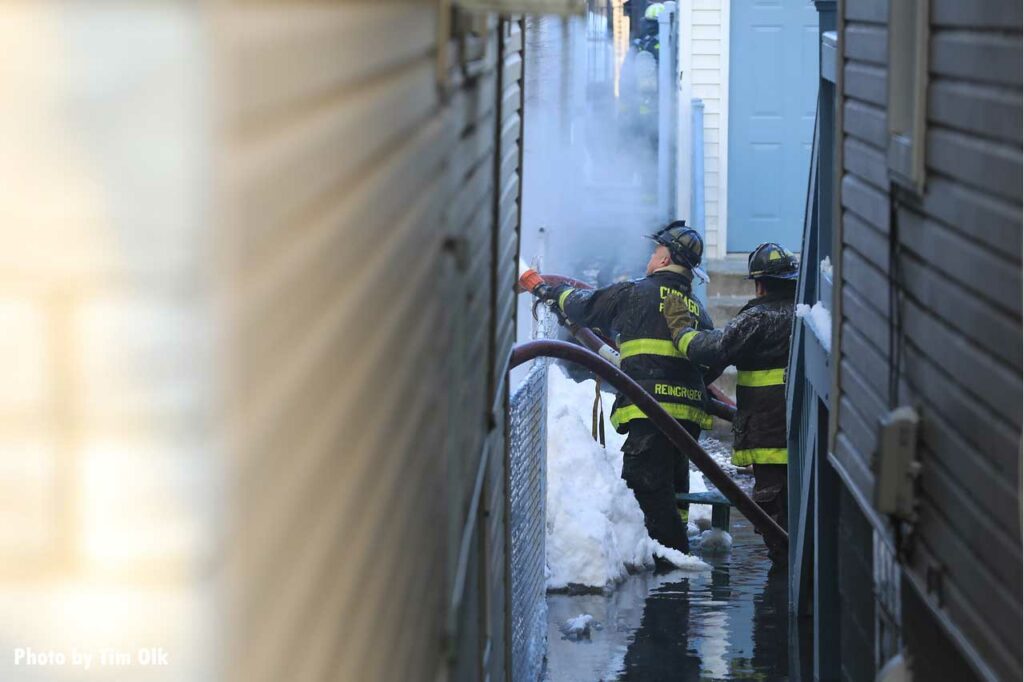 As seen from down an alleyway, Chicago firefighters advance a hoseline