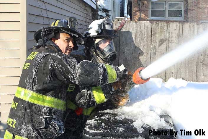 Chicago firefighters, one covered in snow, train a hoseline on the fire building