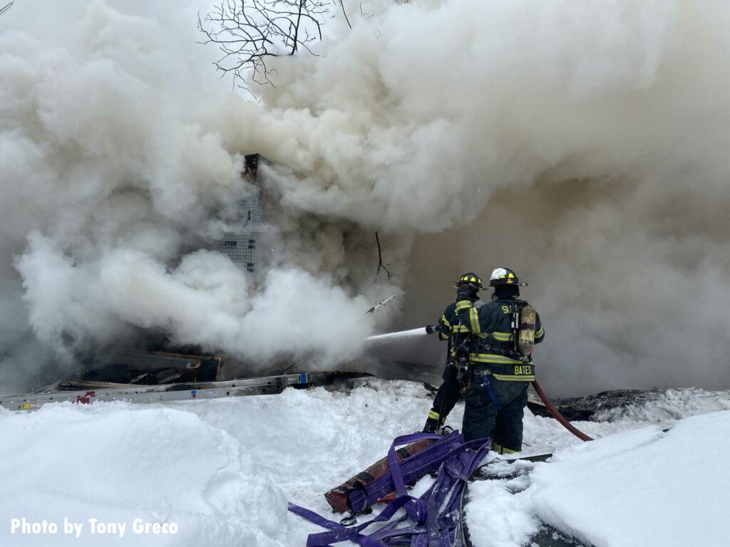 Smoke billows as firefighters train a hoseline on the building