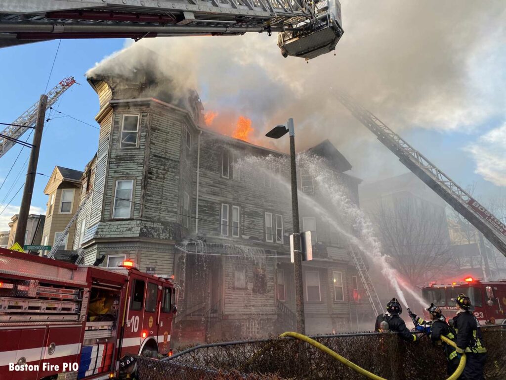 Flames shoot through the roof of the building as firefighters apply water