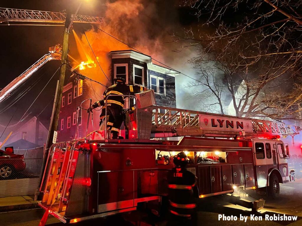 Firefighters with Lynn apparatus and flames coming from building in background