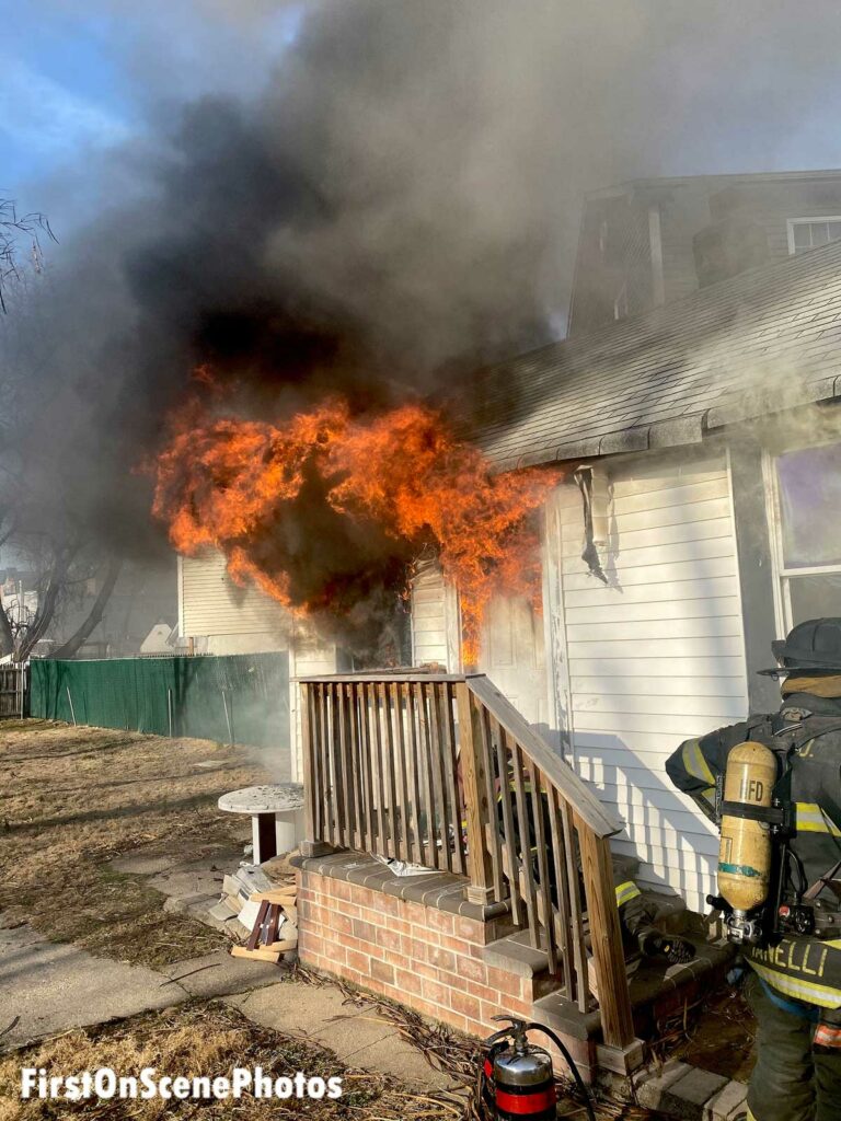 Firefighters on porch as flames blow out a door