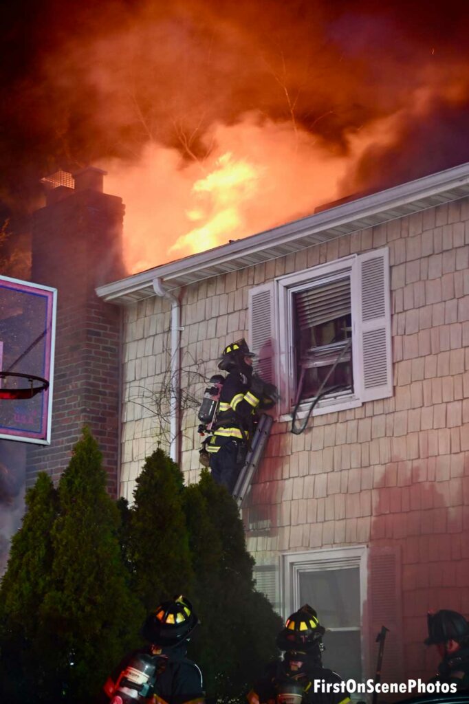 Firefighter on a ladder takes a window as flames rage overhead