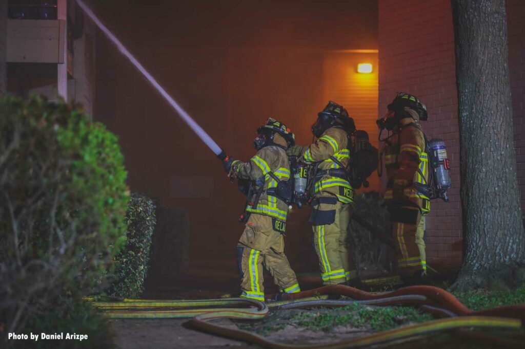 Three firefighters direct a hoseline on the exterior of the complex