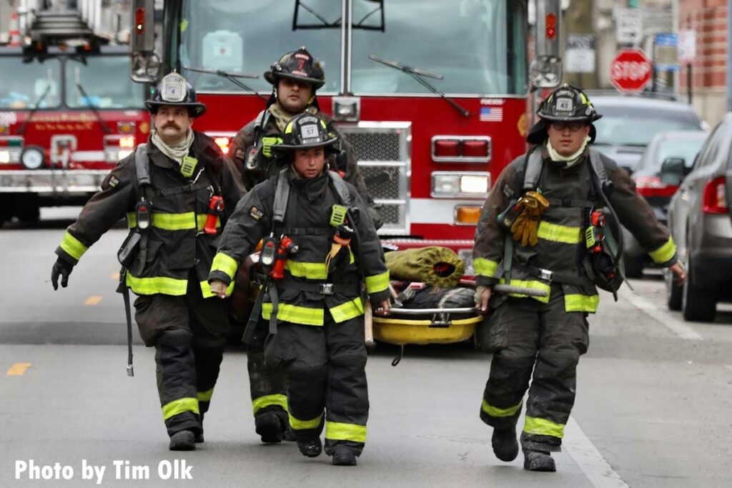 Four Chicago firefighters carry a stokes basket laden with gear from a rig