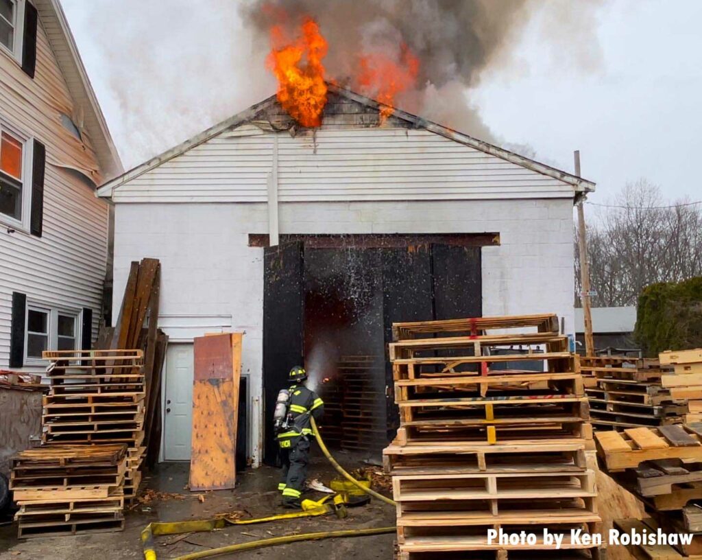 Firefighter directs a hose stream into a building with fire along roofline