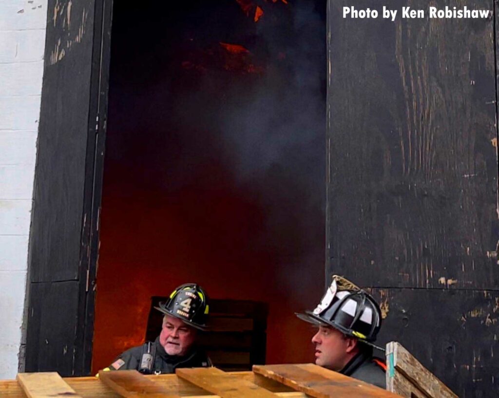 Two firefighters outside the doors of the garage with smoke showing