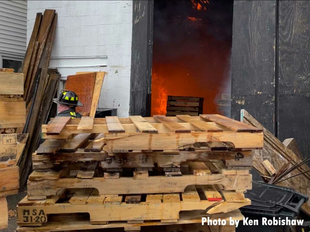 Firefighter with pallets as flames reflect in the interior of the building