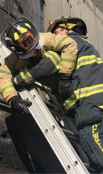 Firefighters should slide their hands down the back of the rails so they don’t lose contact with the ladder while transporting a victim.