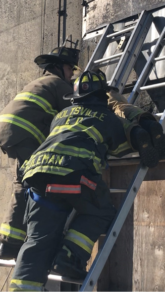 A firefighter operating on an adjoining ladder is trying to support the victim and take some of the weight off the firefighter carrying the bulk of the victim’s weight.