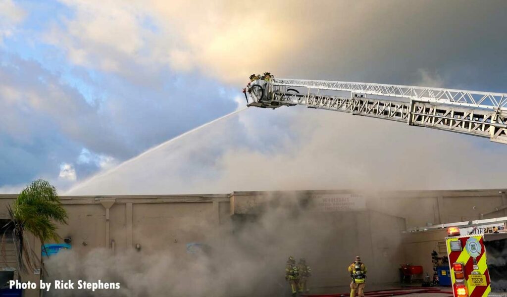 Firefighters in a tower ladder bucket with elevated master stream at warehouse fire