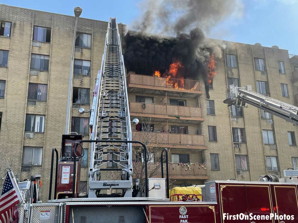 Flames and black smoke billow from the upper floor of an apartment with an aerial ladder reaching to the roof