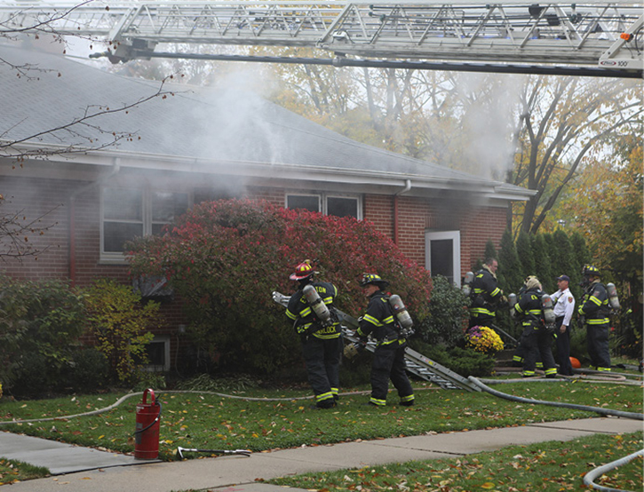 Firefighters raise a portable ladder to the roof to begin roof ventilation as the engine prepares to advance a second line in the front door of the building. Photos by Tim Olk.