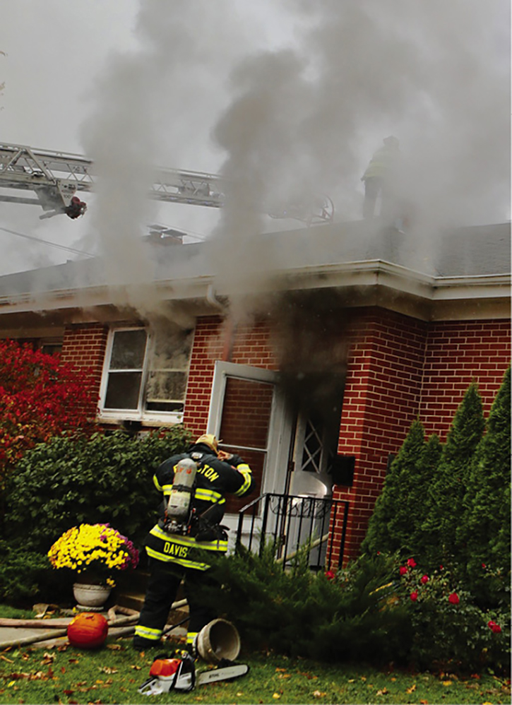 Firefighters have entered the building to begin fire attack. Search crews are also in the building doing a primary search. Note the heavy smoke at the front windows. Members on the roof start to cut the roof.