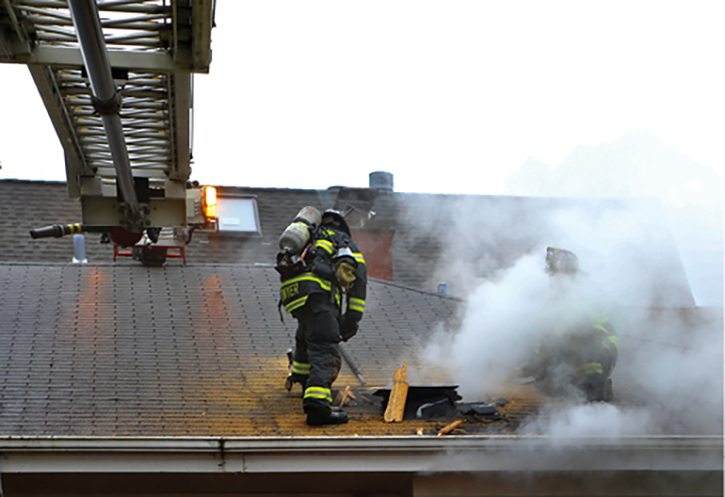 The firefighters on the roof are working on enlarging their hole and checking conditions in the attic space. The skylight is on the exposure C building’s roof, not the fire building.