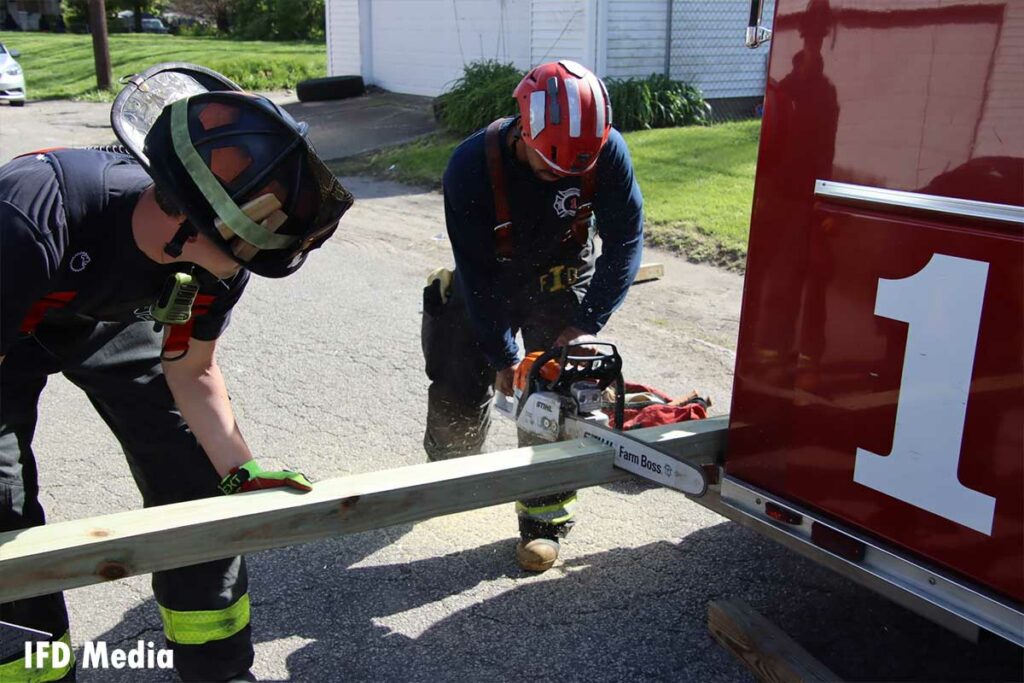 Firefighters use a chainsaw to cut wood on the back of the vehicle