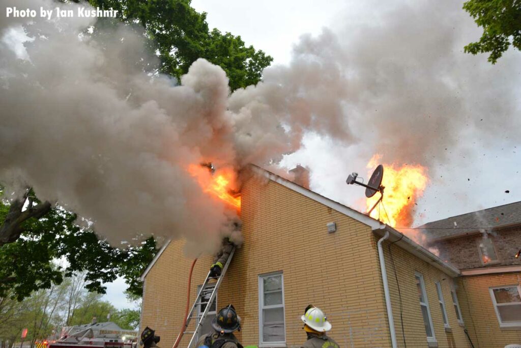 Flames shoot from a window and roof of a home