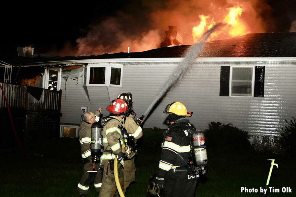 Firefighters train hosestream on flames emanating from roof at house fire in Danville, Iowa