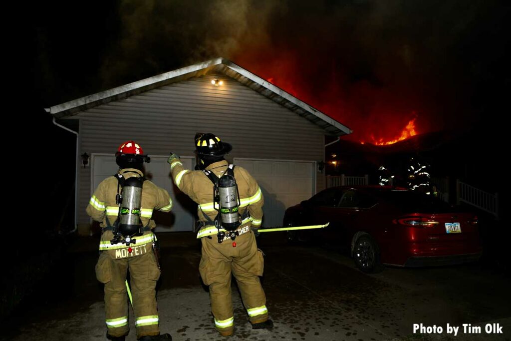 Two firefighters, one with a hook, at house fire