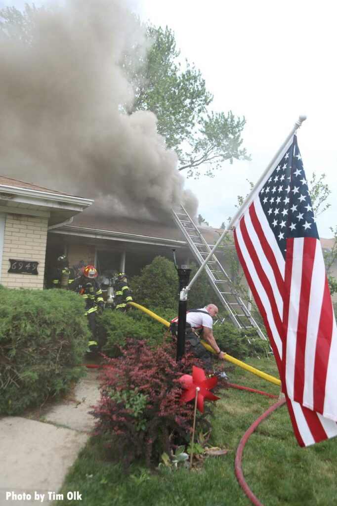 U.S. Flag with firefighters putting a hoseline into the interior of a burning home