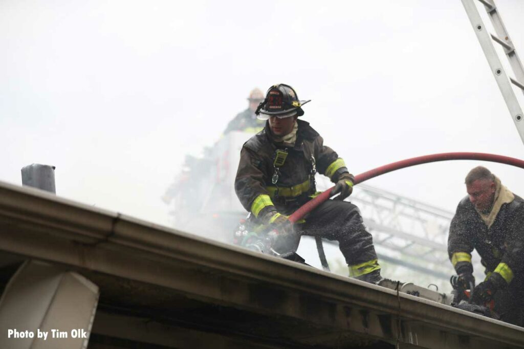 Firefighter on the roof puts a hoseline through the roof