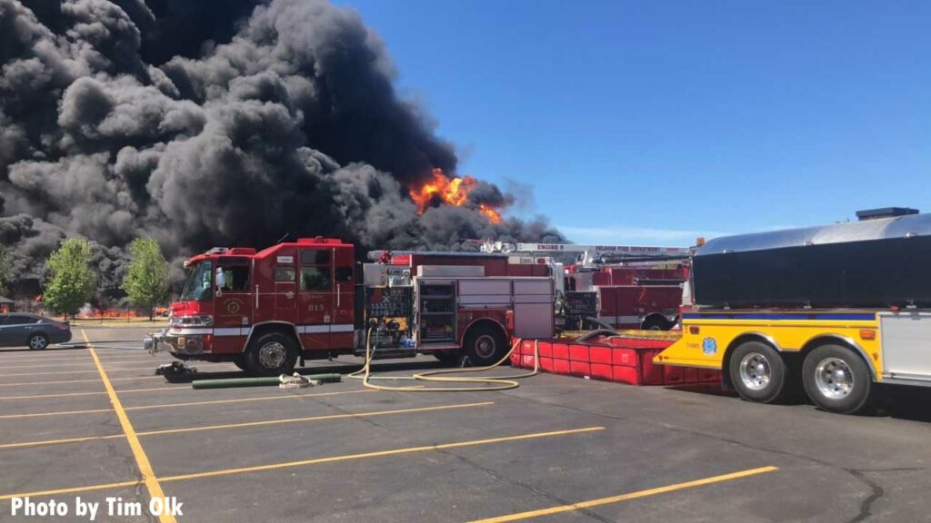 Flames and smoke cloud the sky as fire trucks use portable water tanks