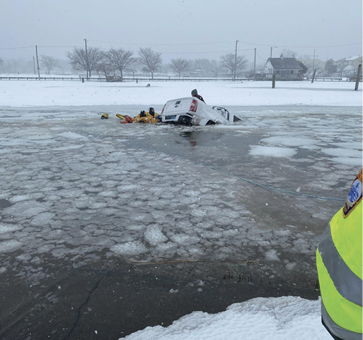 Three fire department rescue swimmers approach the truck and assist the female driver, who is standing in the rear cargo bed.