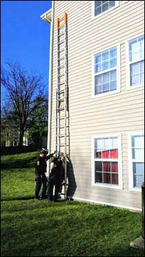 Staged photo of two firefighters butting a ladder against a building