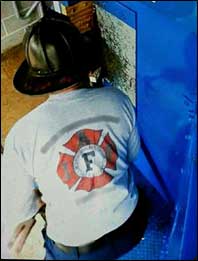 Staged photo of firefighter using a halligan and wedge, forcing the door solo.