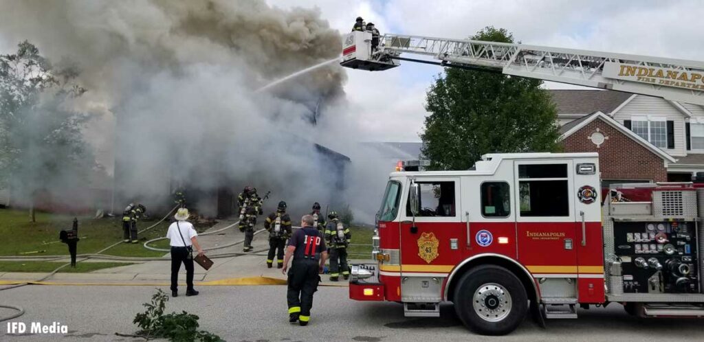 Firefighters train an elevated master stream from a tower ladder bucket on the exterior of a burning home