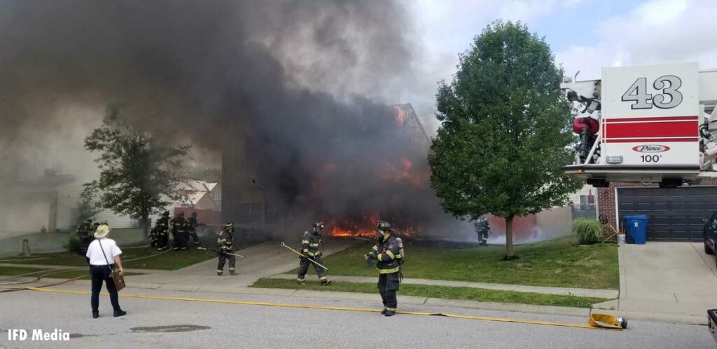 Flames a dark smoke from a house fire in Indianapolis with firefighters in the foreground