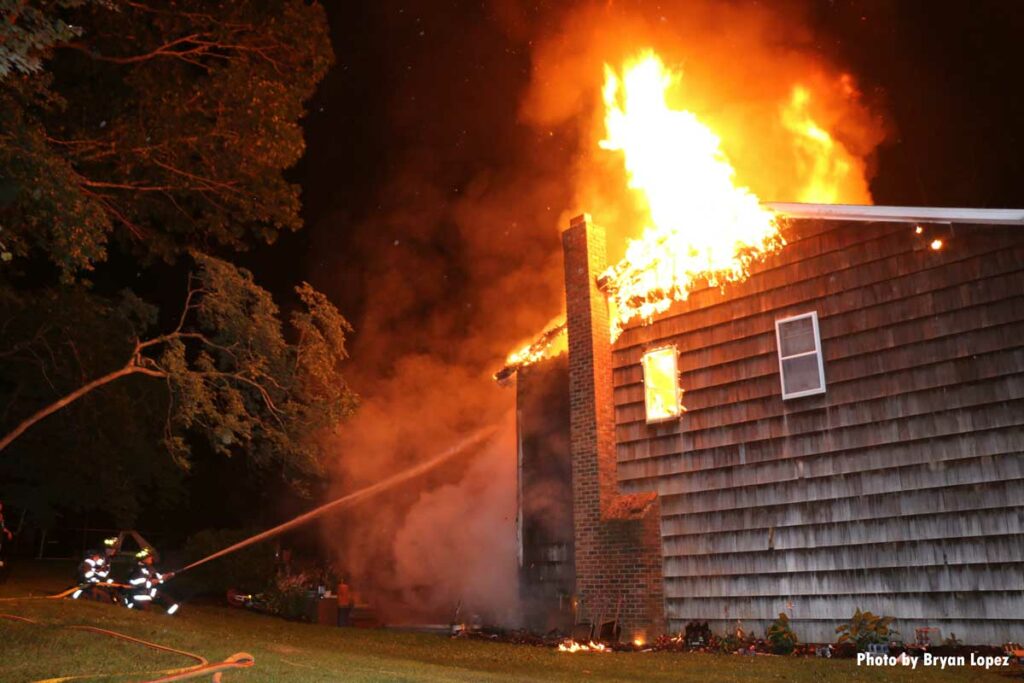 Firefighters train a hoseline on the burning exterior of a Long Island home